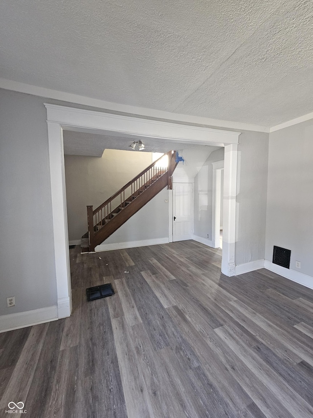 unfurnished living room featuring dark wood-style flooring, stairway, baseboards, and a textured ceiling