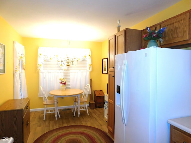 kitchen with white fridge with ice dispenser, light wood finished floors, brown cabinetry, and light countertops