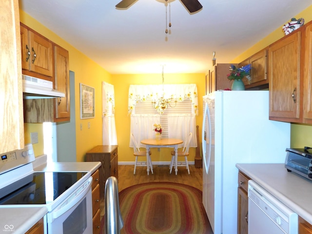 kitchen with white appliances, brown cabinetry, decorative light fixtures, light countertops, and under cabinet range hood