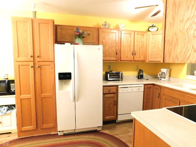 kitchen with a toaster, white appliances, a sink, light countertops, and light wood-type flooring