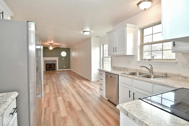 kitchen with light wood-style flooring, stainless steel appliances, a textured ceiling, a fireplace, and a sink