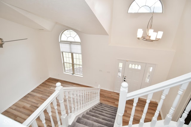 foyer entrance featuring high vaulted ceiling, a notable chandelier, wood finished floors, baseboards, and stairway