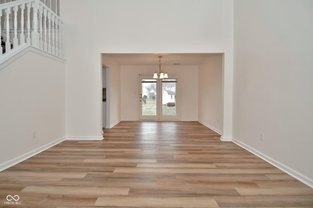 entryway with a towering ceiling, baseboards, a chandelier, and wood finished floors