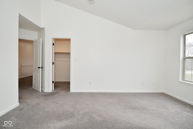 unfurnished bedroom featuring a spacious closet, baseboards, vaulted ceiling, and carpet flooring