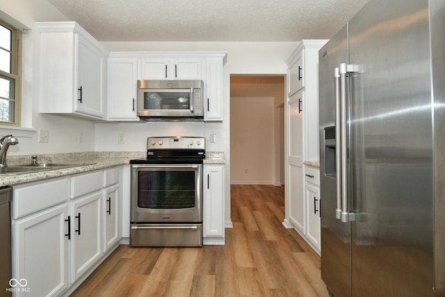 kitchen featuring appliances with stainless steel finishes, light wood-style floors, white cabinets, a sink, and a textured ceiling