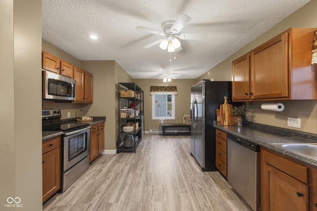 kitchen with brown cabinets, dark countertops, appliances with stainless steel finishes, light wood-style floors, and a textured ceiling