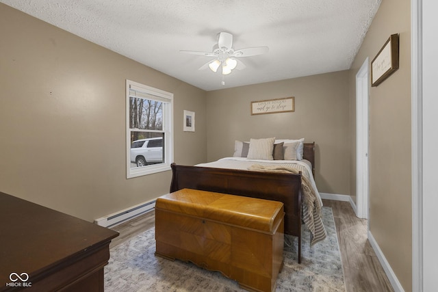 bedroom with baseboard heating, light wood-style floors, ceiling fan, a textured ceiling, and baseboards