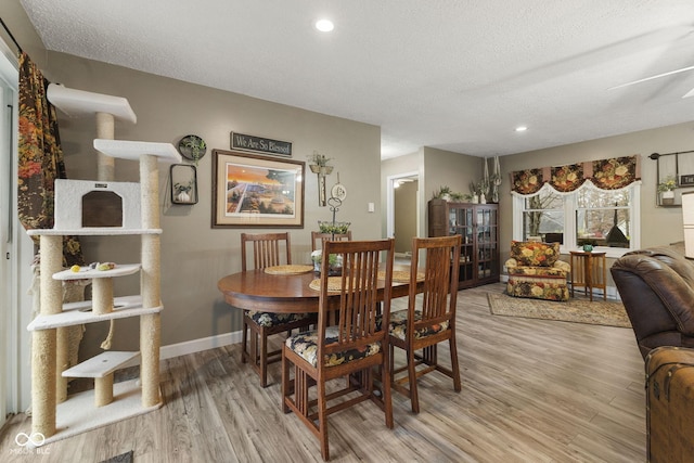 dining space with light wood-type flooring, a textured ceiling, baseboards, and recessed lighting