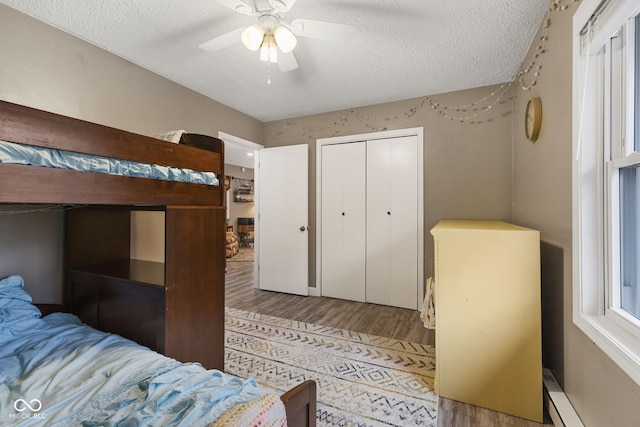 bedroom featuring a baseboard radiator, a closet, ceiling fan, a textured ceiling, and wood finished floors