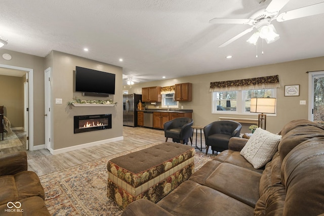 living area featuring light wood-style floors, ceiling fan, a textured ceiling, and a glass covered fireplace