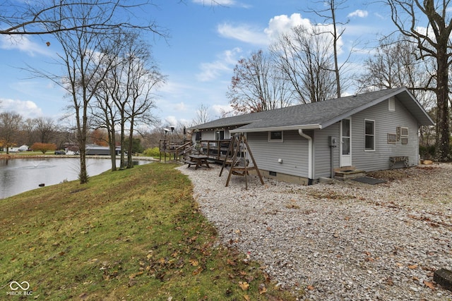 back of property with entry steps, roof with shingles, crawl space, a deck with water view, and a yard