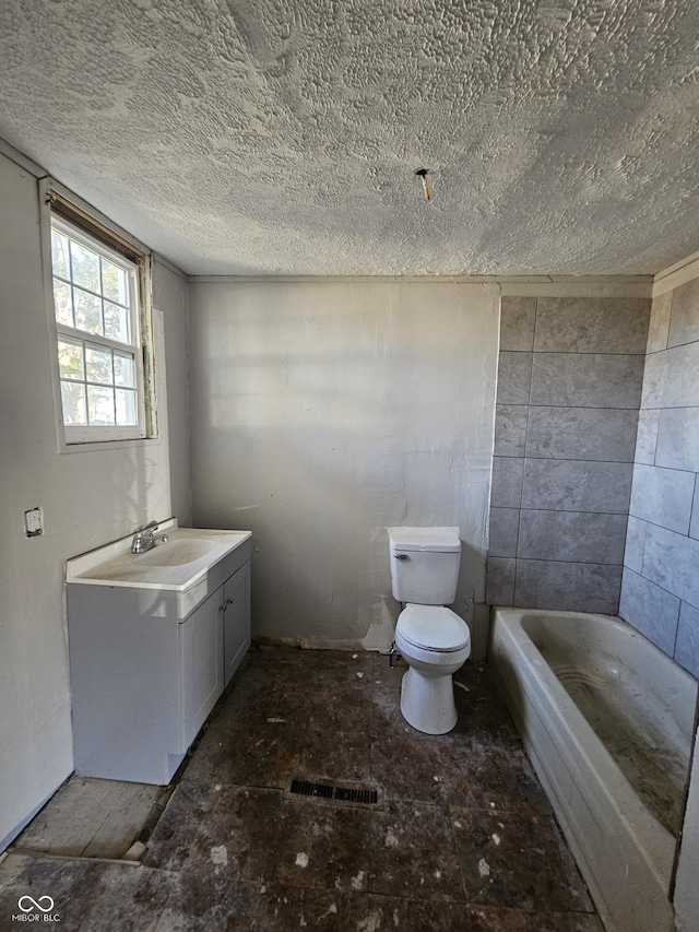 full bath featuring a textured ceiling, a tub to relax in, vanity, and toilet