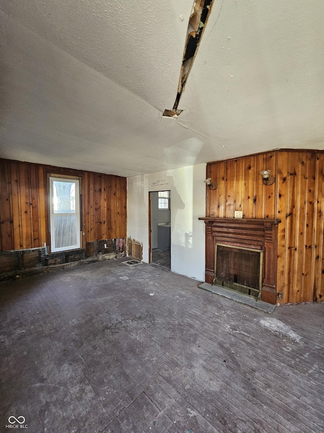 unfurnished living room featuring a fireplace with raised hearth, wood walls, and a textured ceiling