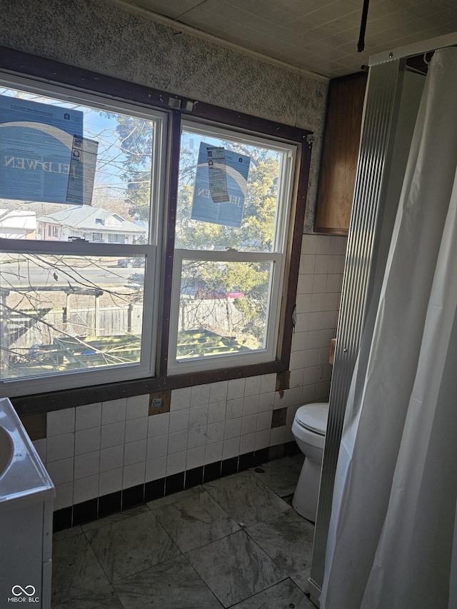 bathroom with toilet, vanity, and tile walls