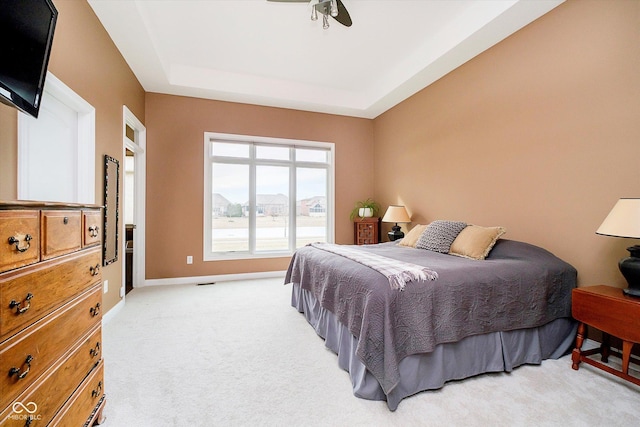 bedroom featuring baseboards, a tray ceiling, a ceiling fan, and light colored carpet