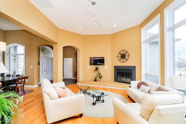 living room with arched walkways, light wood-type flooring, a glass covered fireplace, and baseboards