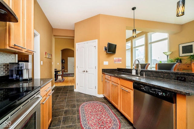 kitchen featuring arched walkways, appliances with stainless steel finishes, a peninsula, a sink, and backsplash