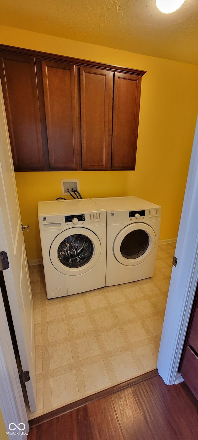 laundry area with cabinet space, washing machine and clothes dryer, a textured ceiling, and light floors