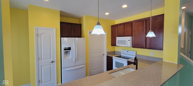 kitchen featuring white appliances, hanging light fixtures, and a peninsula