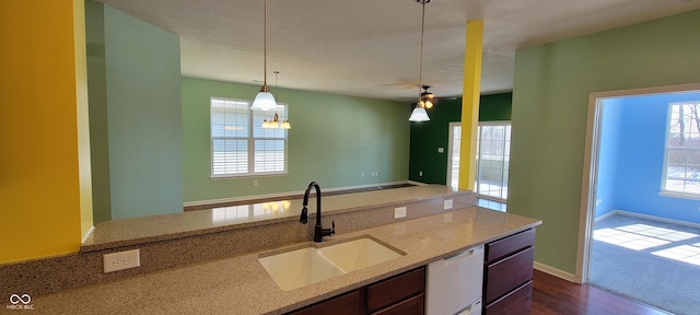 kitchen with dishwasher, light stone counters, dark wood-style flooring, pendant lighting, and a sink