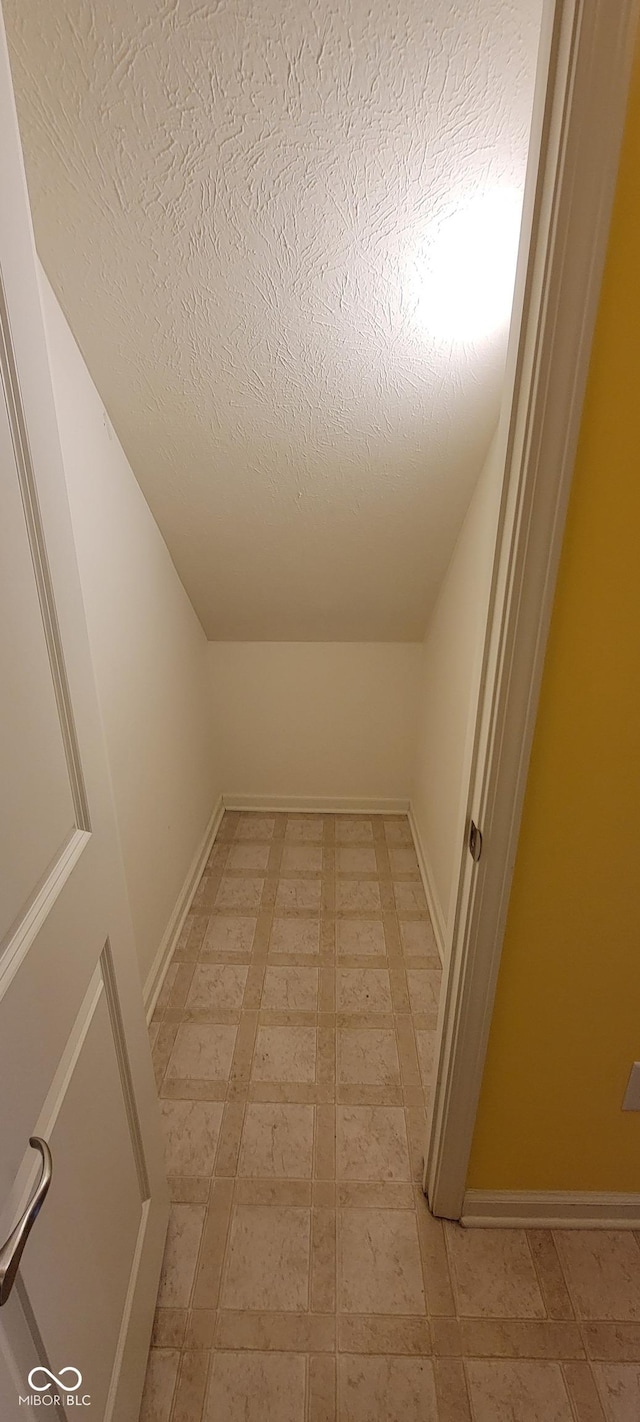 interior space with a textured ceiling, light floors, lofted ceiling, and baseboards