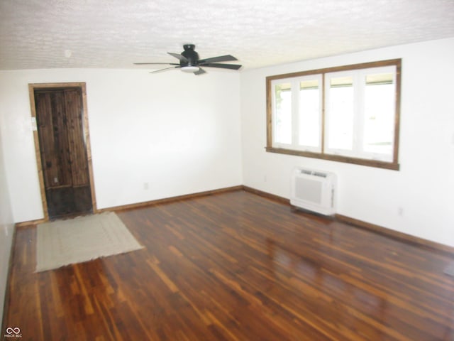 empty room with an AC wall unit, baseboards, a textured ceiling, and dark wood-style flooring