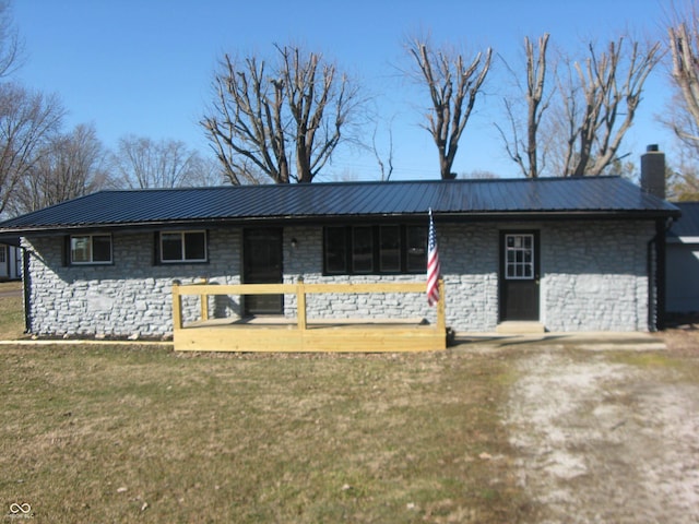 single story home featuring stone siding, a chimney, metal roof, and a front yard