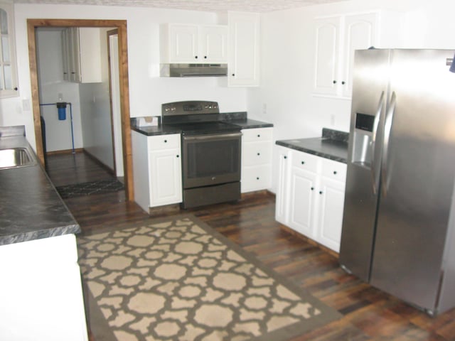 kitchen with dark countertops, appliances with stainless steel finishes, dark wood-type flooring, white cabinets, and under cabinet range hood