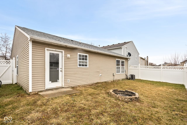 back of property with a shingled roof, a lawn, an outdoor fire pit, central AC, and a fenced backyard