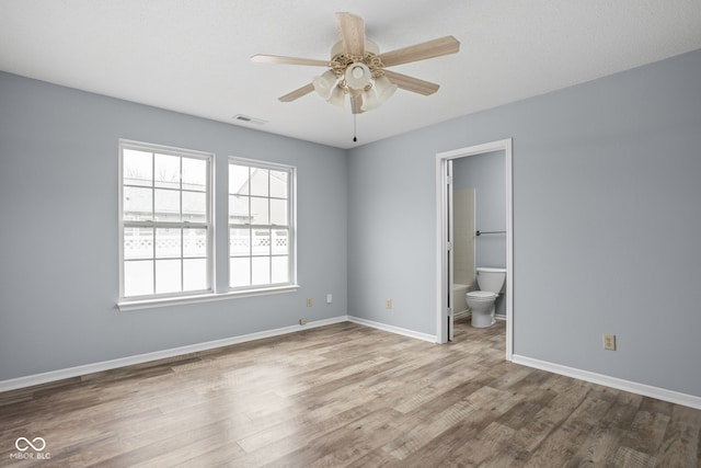 unfurnished bedroom featuring baseboards, connected bathroom, visible vents, and wood finished floors