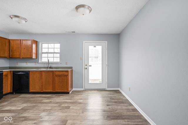 kitchen featuring light wood finished floors, black dishwasher, visible vents, brown cabinetry, and a sink