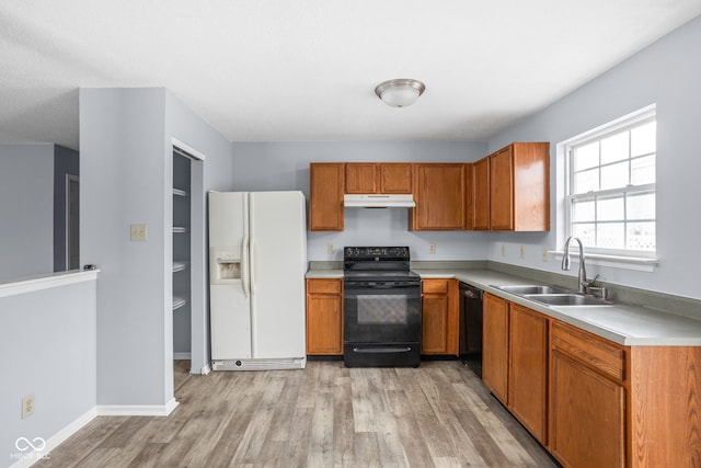 kitchen featuring light wood-style flooring, under cabinet range hood, a sink, light countertops, and black appliances