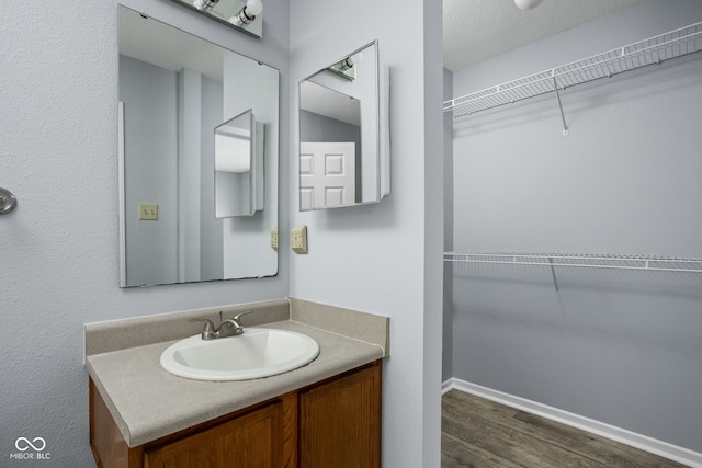 bathroom featuring a walk in closet, vanity, baseboards, and wood finished floors