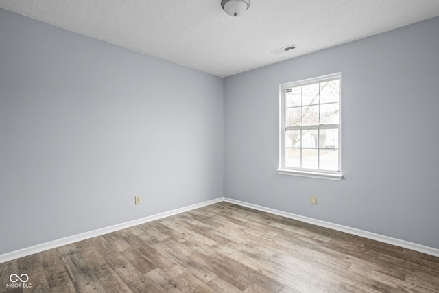 empty room featuring a textured ceiling, wood finished floors, visible vents, and baseboards