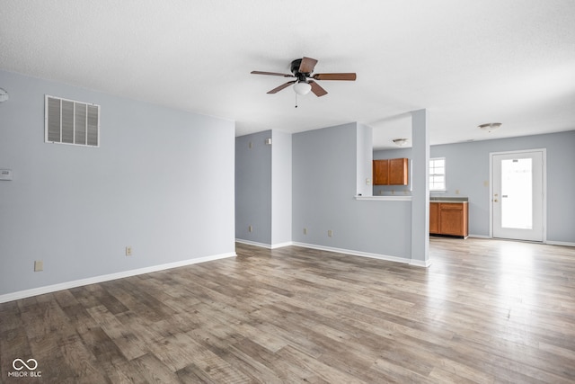 unfurnished living room featuring baseboards, wood finished floors, visible vents, and a ceiling fan