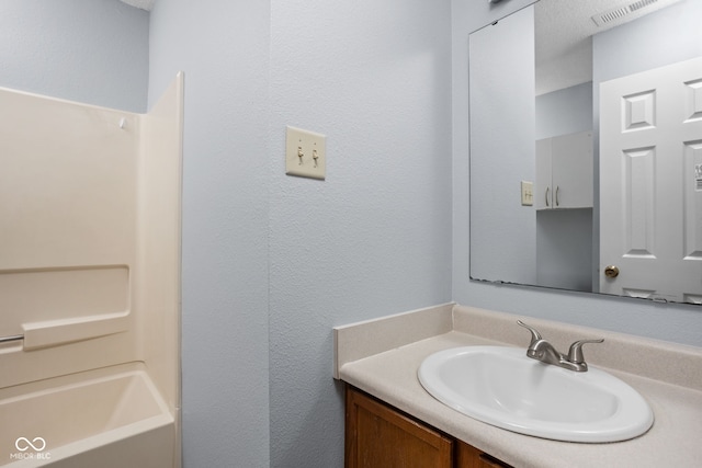 bathroom featuring  shower combination, a textured wall, visible vents, and vanity