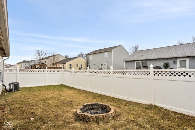 view of yard featuring an outdoor fire pit, central AC unit, a fenced backyard, and a residential view