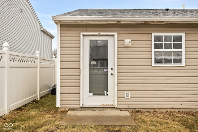 view of exterior entry with fence and roof with shingles