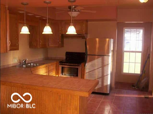 kitchen with a peninsula, a sink, stainless steel appliances, light countertops, and pendant lighting