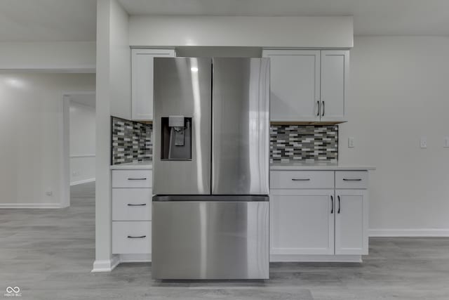 kitchen with light wood-style flooring, white cabinetry, light countertops, backsplash, and stainless steel fridge