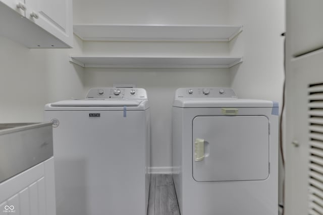 clothes washing area featuring washer and clothes dryer, cabinet space, a sink, wood finished floors, and baseboards