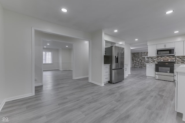 kitchen with light countertops, decorative backsplash, appliances with stainless steel finishes, white cabinets, and light wood-type flooring