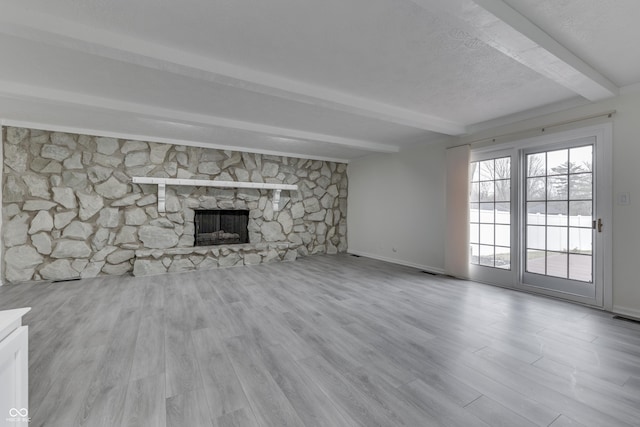 unfurnished living room with light wood finished floors, a stone fireplace, beamed ceiling, and baseboards