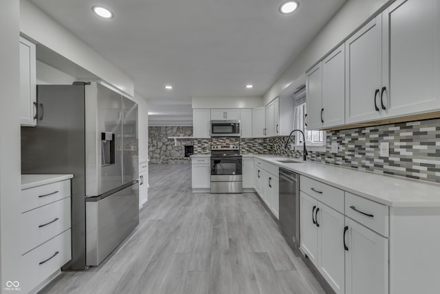 kitchen with stainless steel appliances, a sink, white cabinetry, light countertops, and backsplash