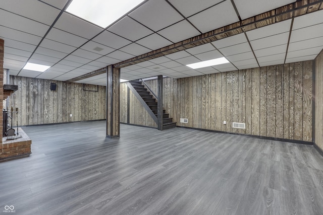 finished below grade area with a paneled ceiling, stairs, visible vents, and wood finished floors