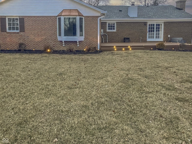 rear view of property with a deck, brick siding, a chimney, and a lawn