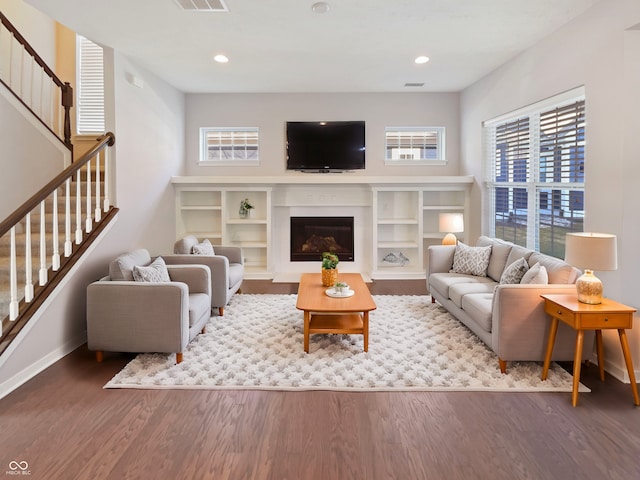 living area with stairs, visible vents, wood finished floors, and a glass covered fireplace