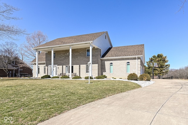 neoclassical / greek revival house featuring brick siding, a front yard, and roof with shingles