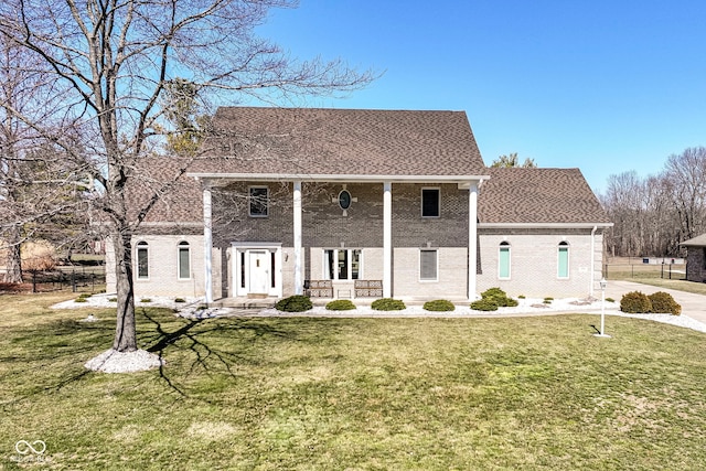 greek revival inspired property with brick siding, covered porch, a front lawn, and roof with shingles