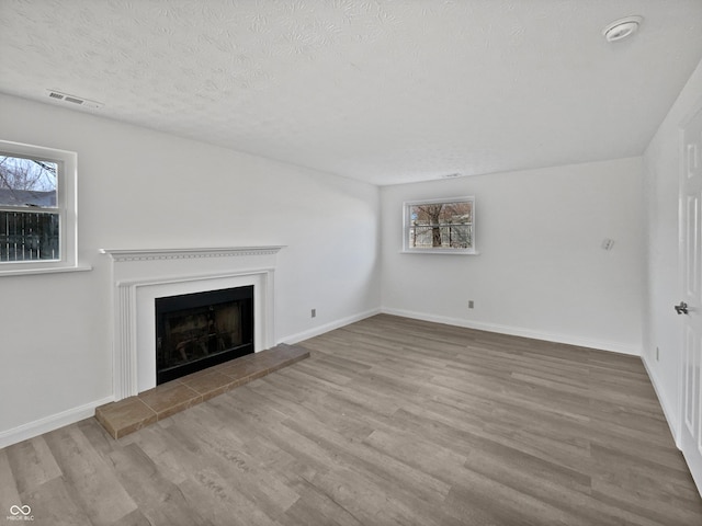 unfurnished living room featuring a fireplace with raised hearth, a textured ceiling, plenty of natural light, and wood finished floors